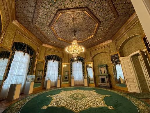 Gilded chandeliers and ornate tiled stoves inside the reception hall of Nurullaboy Palace