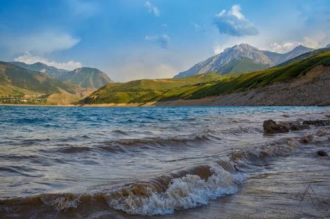 Scenic turquoise waters of Charvak Reservoir surrounded by dry mountain slopes and blue sky
